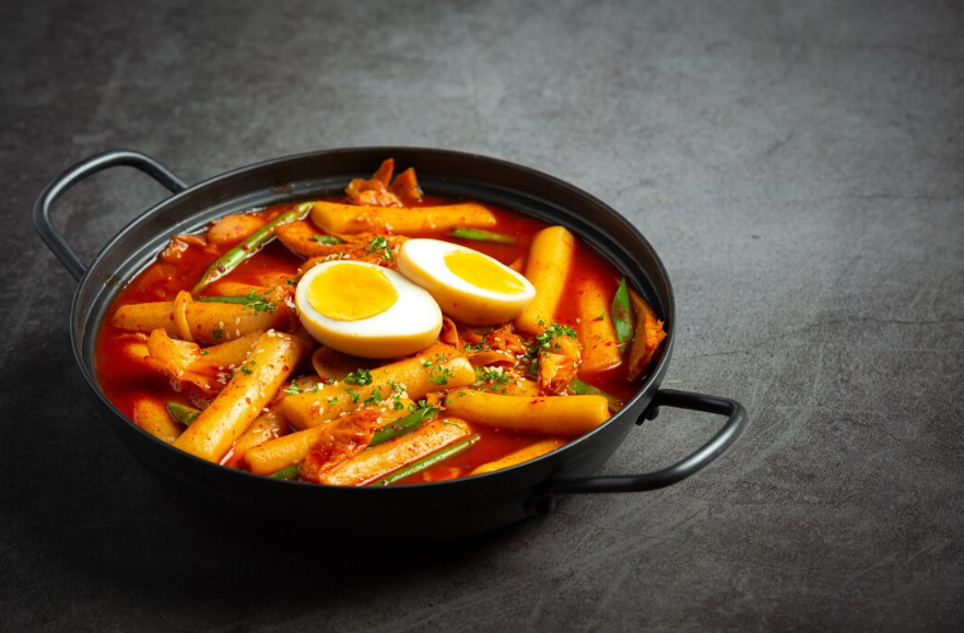 lose-up of a spicy tteokbokki dish with rice cakes, fish cakes, and boiled eggs in a rich red sauce