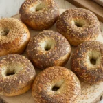 Fresh sourdough bagels on a wooden board with seeds and grains