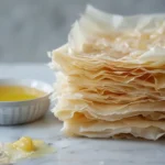 Filo pastry sheets being layered with butter on a work surface